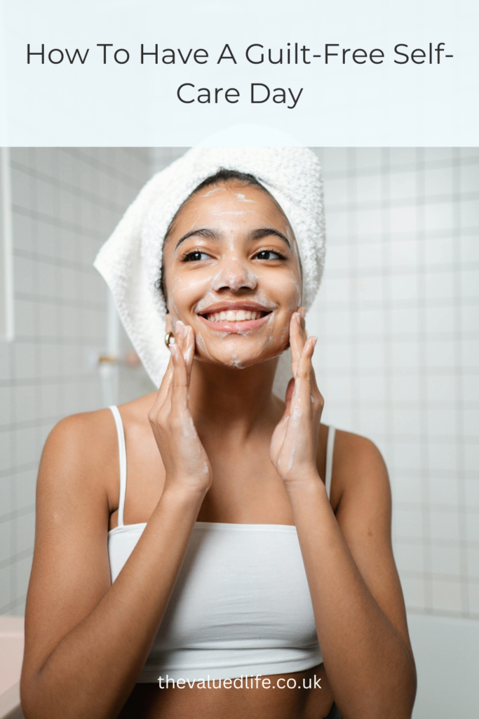 Woman washing her face with a towel wrapped around her hair. Title overlay says' How To Have A Guilt-Free Self-Care Day'