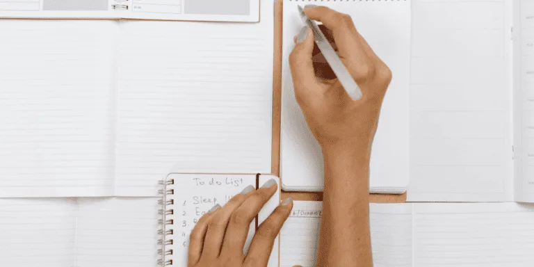 4 open notebooks with a hand holding a pen to symbolise goal-setting and planning. -values driven goals