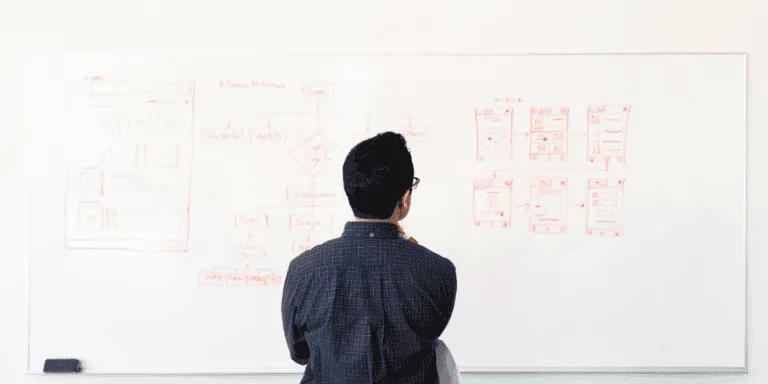 Man Wearing Blue Dress Shirt Facing Whiteboard looking at a diagram to symbolise comparison of the difference between values and goals