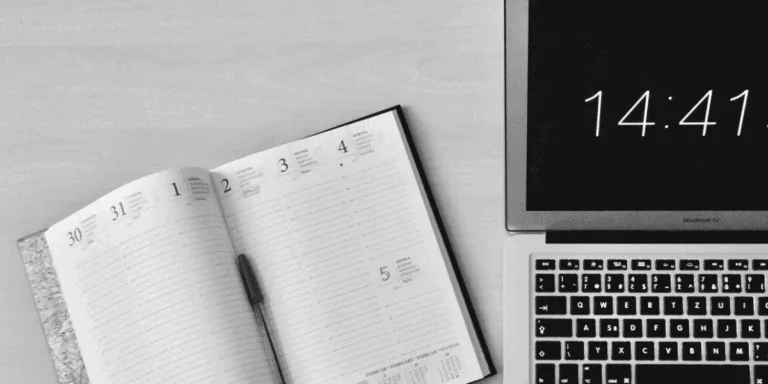 Open calendar or diary next to a laptop screen with the time on it to plan out a productivity sprint