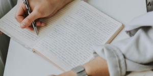 Person Writing in a one line a day journal While Holding Coffee Mug