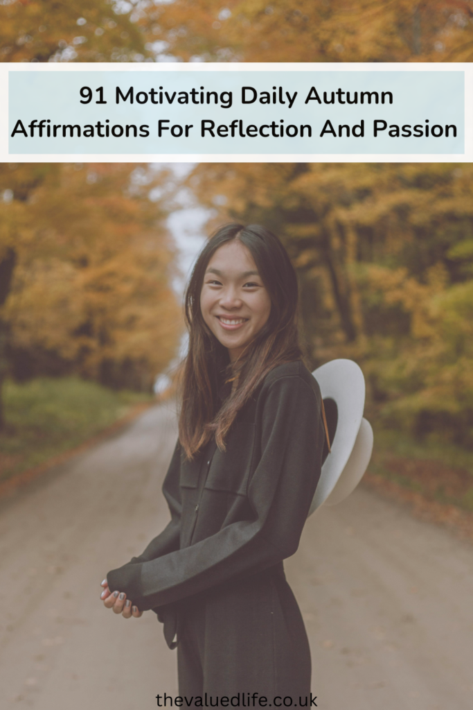 Smiling Woman Standing on a Dirt Road surrounded by trees with amber leaves to symbolise autumn affirmations