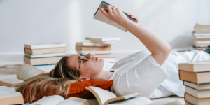 Woman reading book on floor surrounded by books. How to become a more diligent person