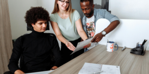 Woman in Green Tank Top pointing out something on a sheet of paper to two men to show how to handle criticism as a perfectionist