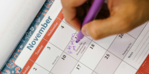 Person Holding Purple Click Pen writing on a calendar page for november journal prompts