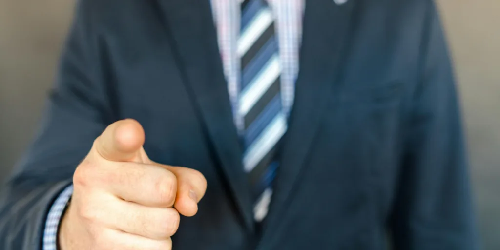 Close-up of a person in a suit pointing directly at the camera, symbolizing choosing the wrong individual for a delegated task.