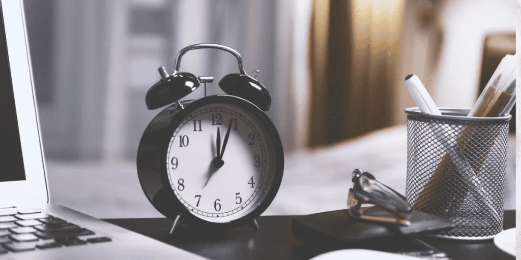 Classic alarm clock on a desk next to a laptop and stationery, symbolizing time management strategies to combat procrastination, in line with the 'lazy perfectionist' mindset