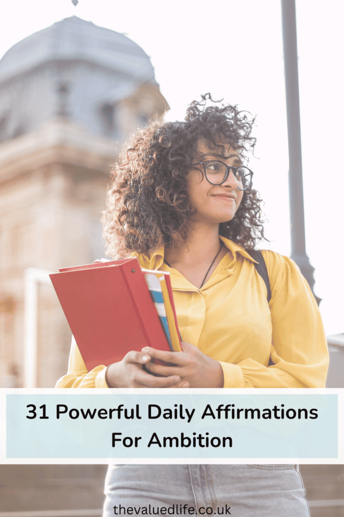 Young woman in a yellow blouse holding notebooks and looking ahead confidently, with overlay text reading '31 Powerful Daily Affirmations For Ambition' and website link 'thevaluedlife.co.uk' at the bottom. This image highlights the theme of ambition, aligning with daily affirmations for achieving goals and self-growth