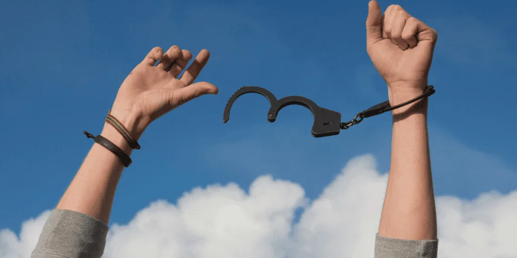 Hands breaking free from open handcuffs against a blue sky, symbolizing breaking free from the perfectionism-procrastination loop