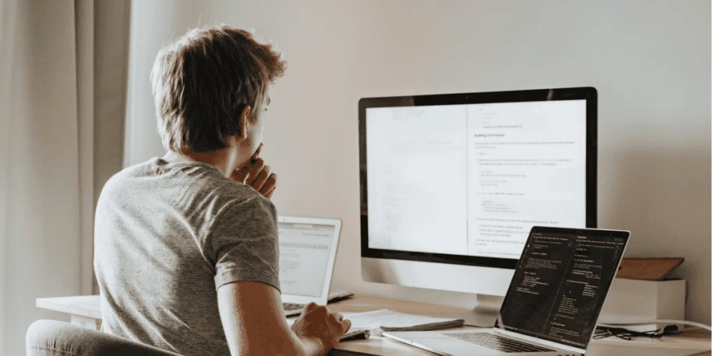 Person working at a desk with multiple screens, illustrating the decision to delegate or drop tasks as a strategy to manage perfectionism and procrastination.