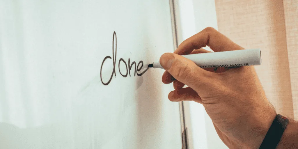 A hand writing the word 'done' on a whiteboard, symbolizing the mantra 'done is better than perfect' as a way to combat the tendencies of a lazy perfectionist.