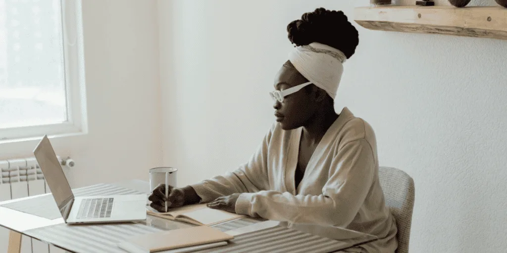 Woman sitting at a desk writing in a notebook, embodying the dedication needed to overcome the 'lazy perfectionist' mentality and enhance productivity