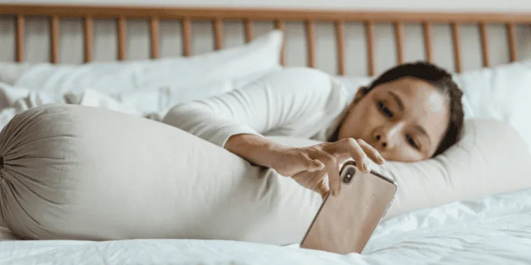 Person lying in bed and scrolling on their phone, symbolizing the struggle of a lazy perfectionist who procrastinates despite high standards.