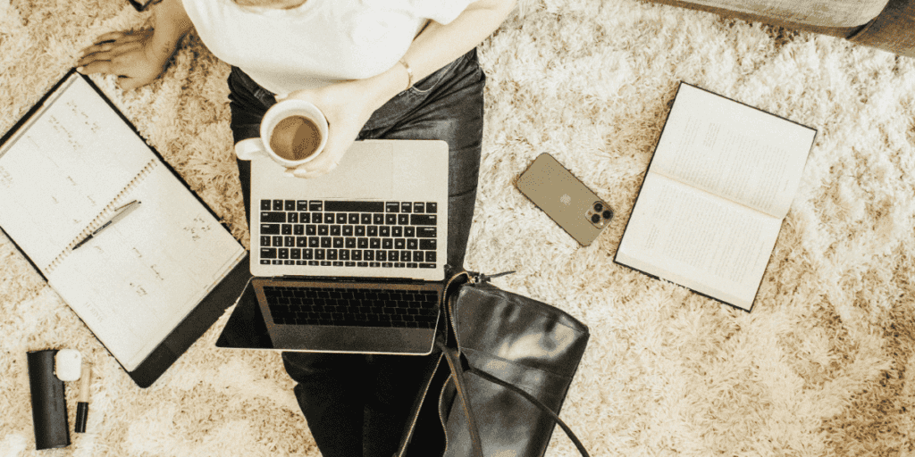 Overhead view of a person sitting on the floor with a laptop, coffee, planner, and books, illustrating the myth of multitasking as an effective productivity strategy