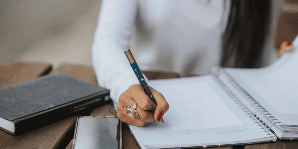 Person writing in a notebook, symbolizing the challenge of overcoming the urge for perfectionism in planning and productivity.