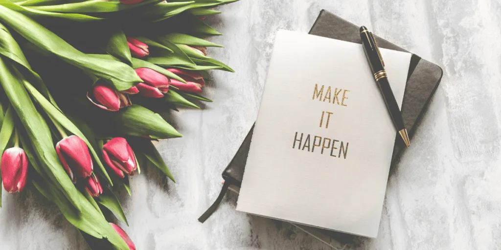 A journal with the phrase 'Make It Happen' next to a pen and a bouquet of tulips, symbolizing the importance of setting clear, actionable goals as a foundational step in healthy striving.