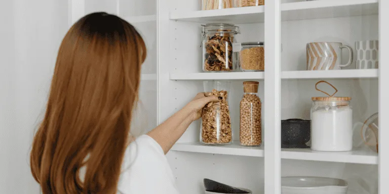 A woman organizing glass jars filled with dry goods in a kitchen pantry, symbolizing productive activities that may disguise secretly procrastinating behaviors. Perfectly arranged shelves suggest a focus on minor tasks over meaningful progress.