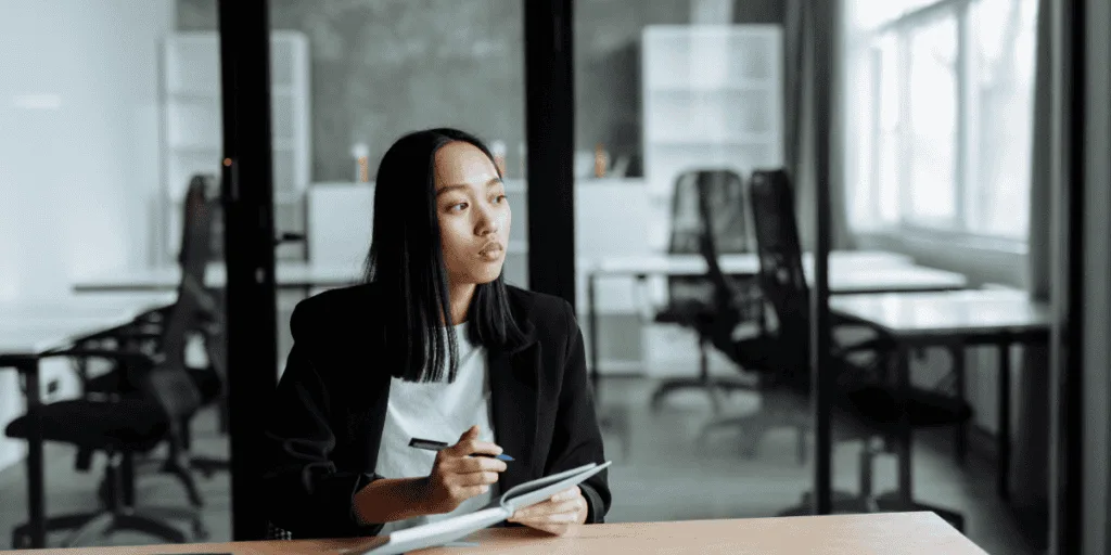 A professional woman in a blazer jotting down notes in a quiet office setting, illustrating a structured weekly planning routine for work productivity.