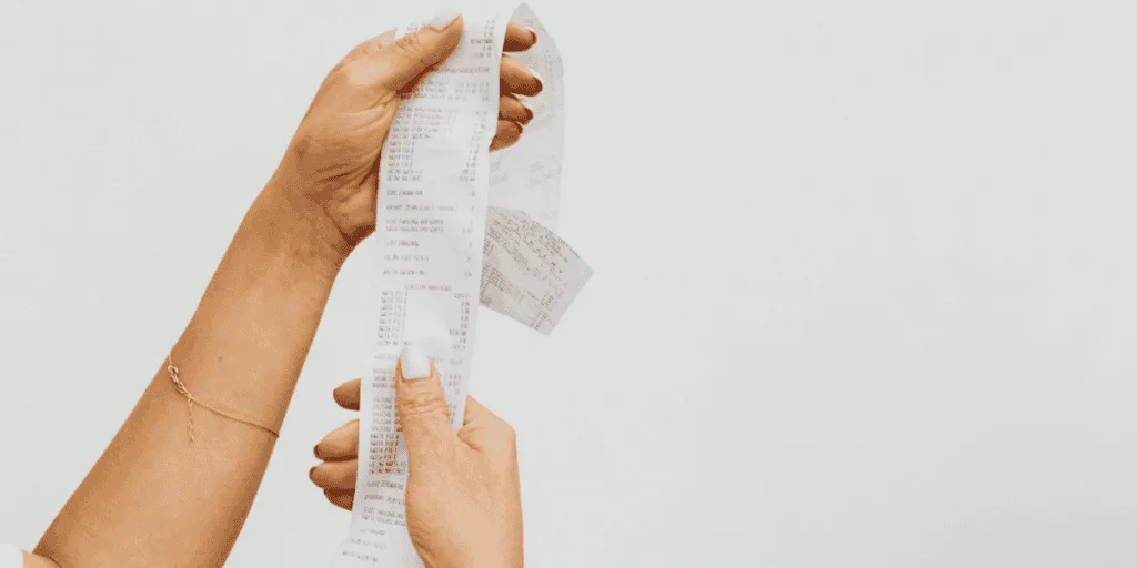 Hands holding a long receipt, representing the hidden costs and burden associated with perfectionistic tendencies.