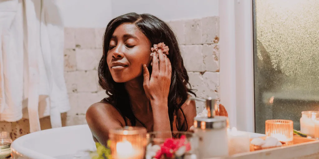 A woman enjoying a luxurious self-care moment in a candle-lit bath, holding a flower to her face with a serene expression. This indulgent scene reflects how frequent pampering might be a subtle form of secretly procrastinating from tackling essential tasks.